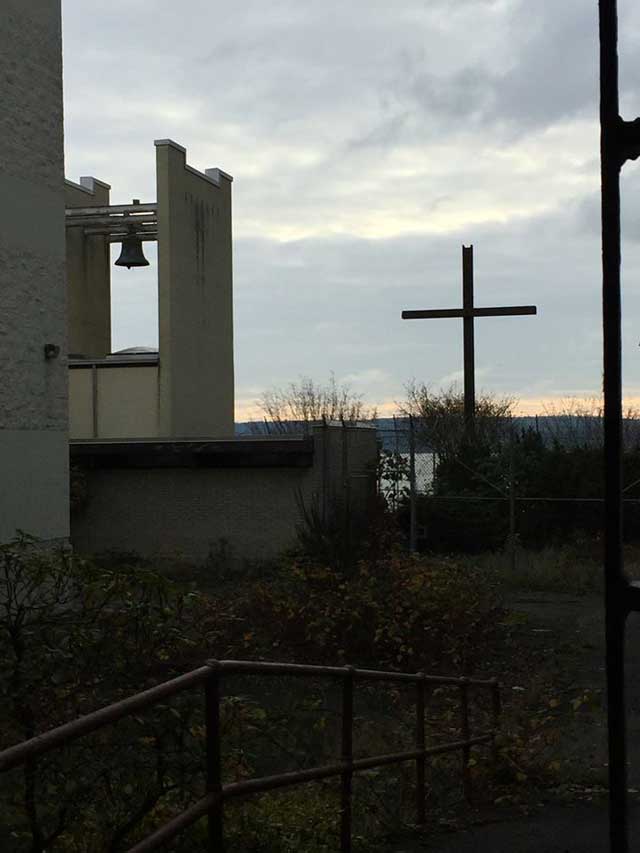 cross and bell outside the chapel of Mount Tahoma with a view of the water.