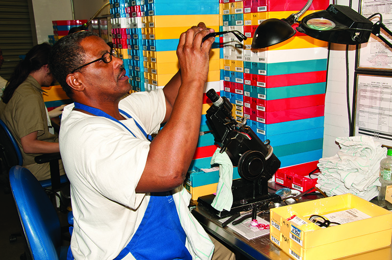 man sitting at a work bench working on optical glasses