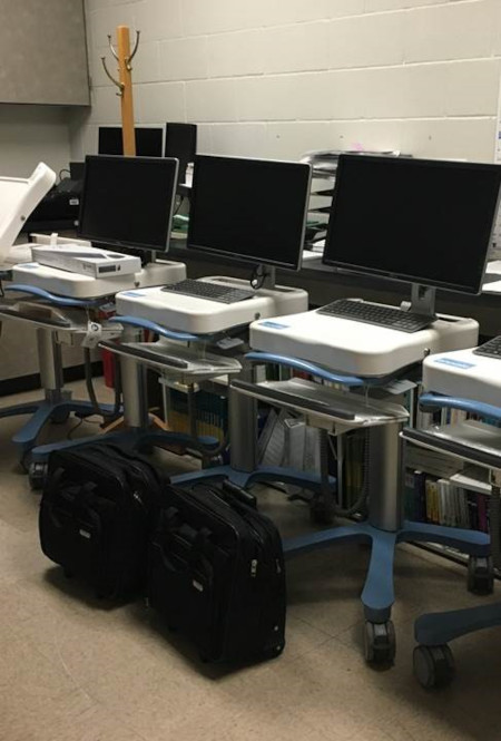 multiple computers on wheels, which are telehealth carts, sit in a room.