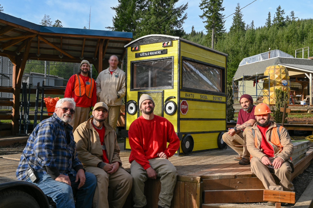 Group of men pose in front of hand built wooden school bus.