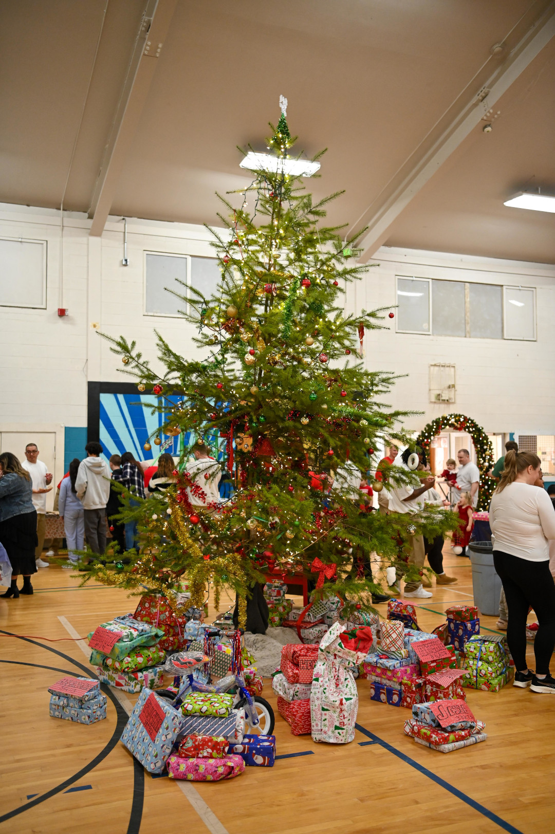 Christmas tree in gymnasium with presents underneath it.