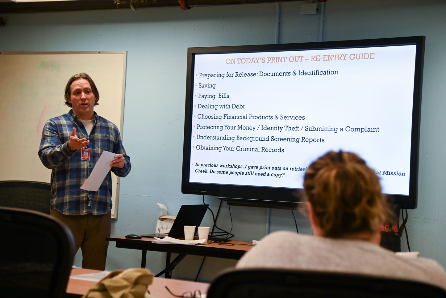 Man at the front of the room, addressing others in the room.