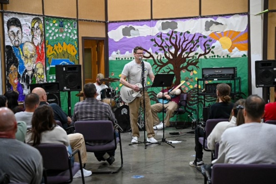 a man plays the guitar in front of a painted wall while people watch