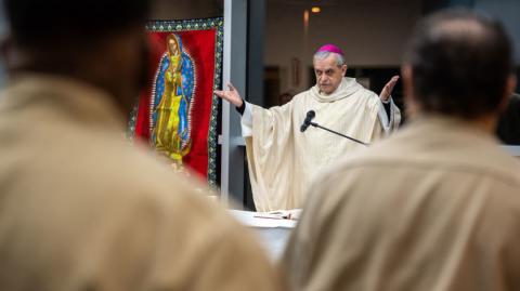 a priest standing behind a microphone with hands up