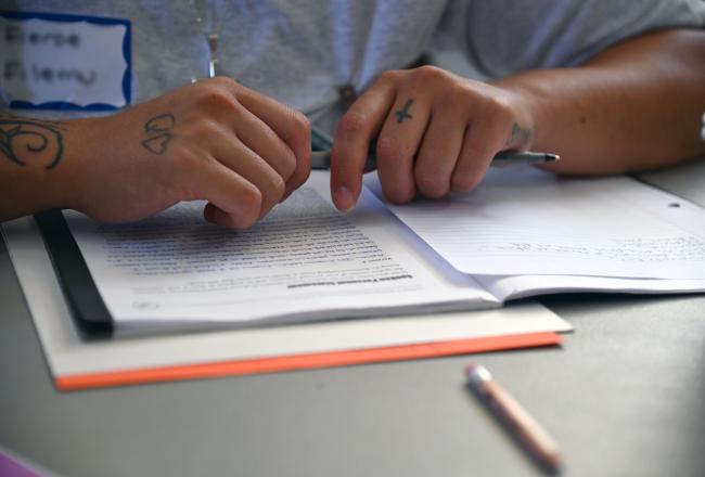 Closeup of a woman’s hands holding a pen on top of a workbook with handwritten notes.